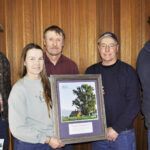 Mark Lewing, left, and Dan Rogers, right, with the Montana Register of Big Trees program, present a framed photograph of the national champion Plains Cottonwood that stands on the property of the Huls Dairy near Corvallis. Trudy and Tim Huls and Dan Huls are shown accepting the photo, which is also featured on the front cover of the 2014 National Register of Big Trees Calendar.