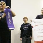 LeAnn Dolly-Powell holds one of the banners signifying an accomplishment of Project UNIFY while Jon Wilson holds the main banner and Chris Clare looks on during an assembly at Victor School. Jean Schurman photo.